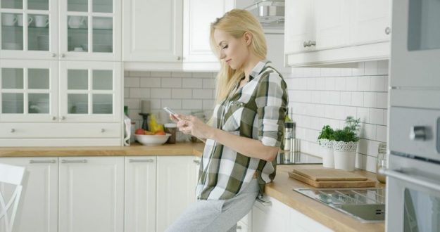 Is My House Solar Ready A woman using her cellphone on the kitchen