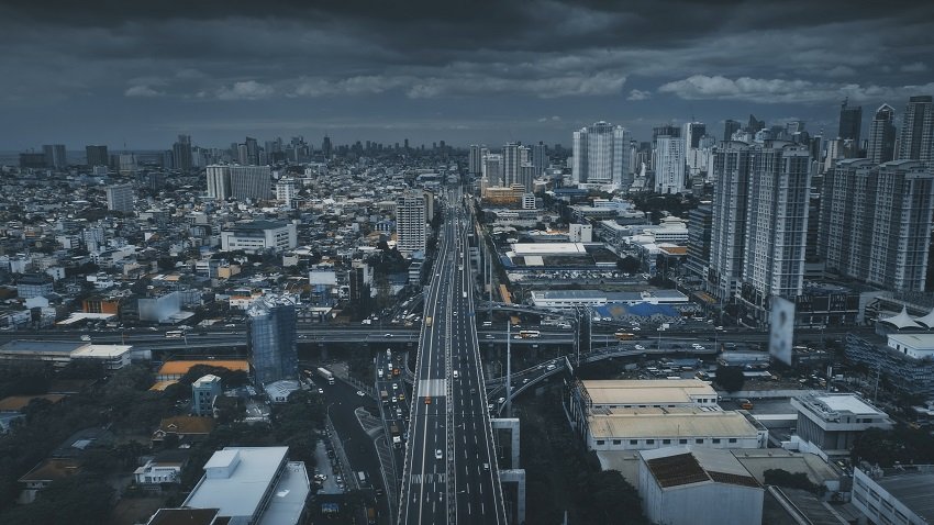 Traffic road with cars and trucks at urban street aerial. High skyscrapers, buildings at cityscape of Philippines metropolis of Manila. Cinematic vehicle transportation in dramatic tones